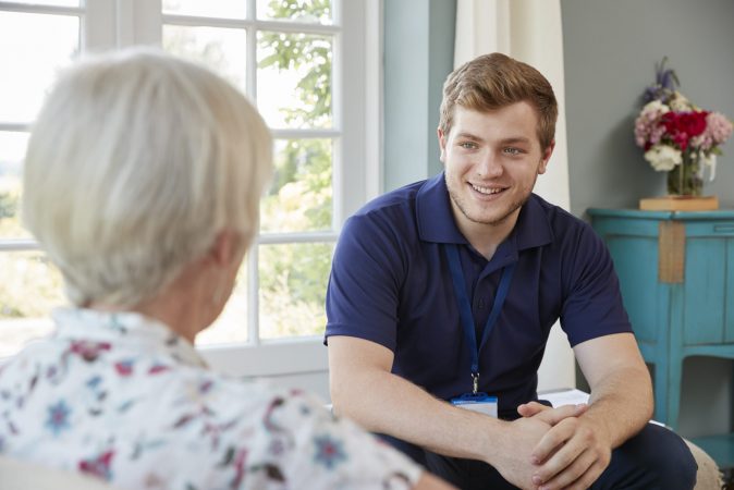 Senior woman talking with male care worker on home visit